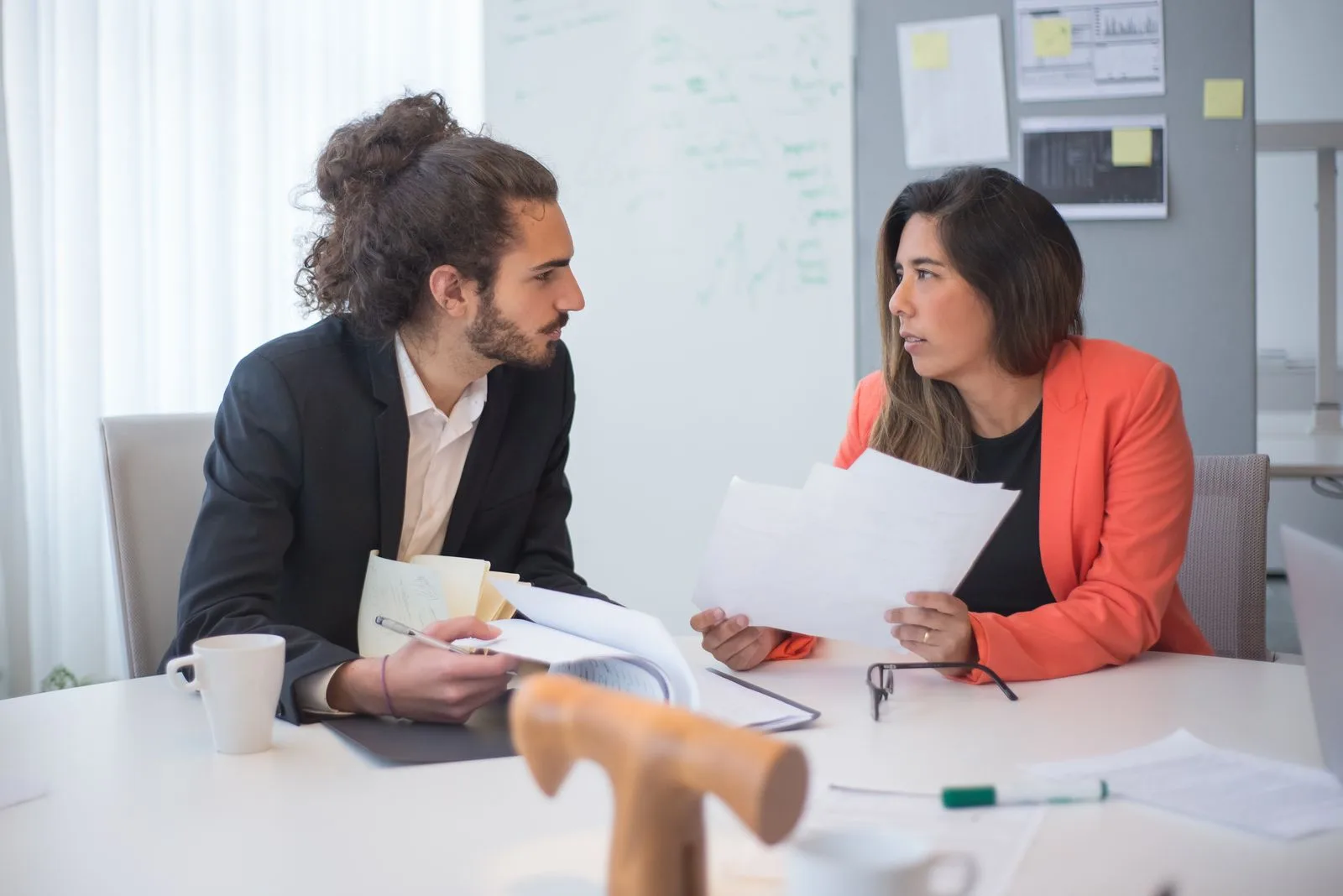 Two colleagues engaged in a discussion at an office table with documents and coffee