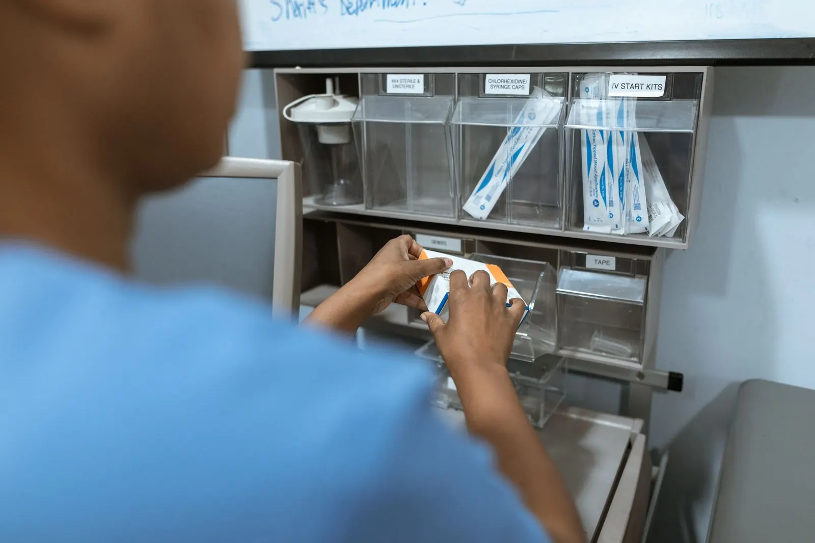 A clinician taking a packaged item from labelled supply bins on a clinic wall