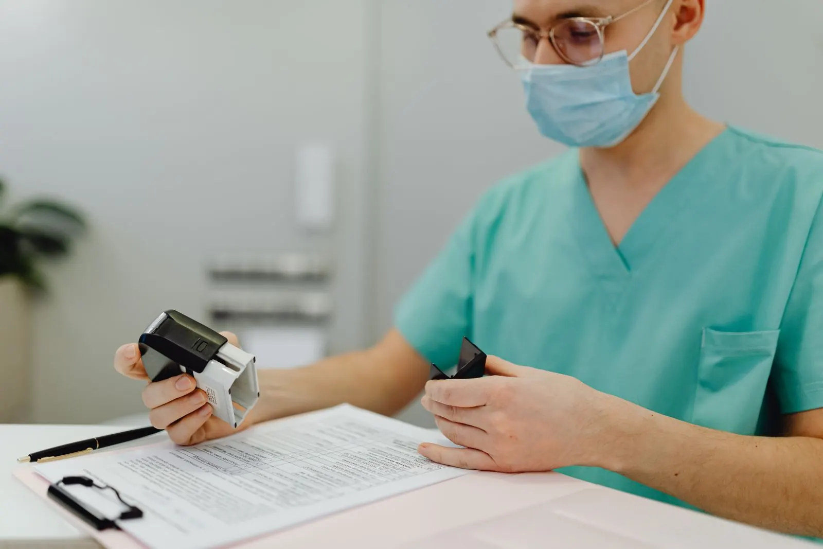 A clinician in scrubs working on paper forms on a clipboard with a handheld scanner