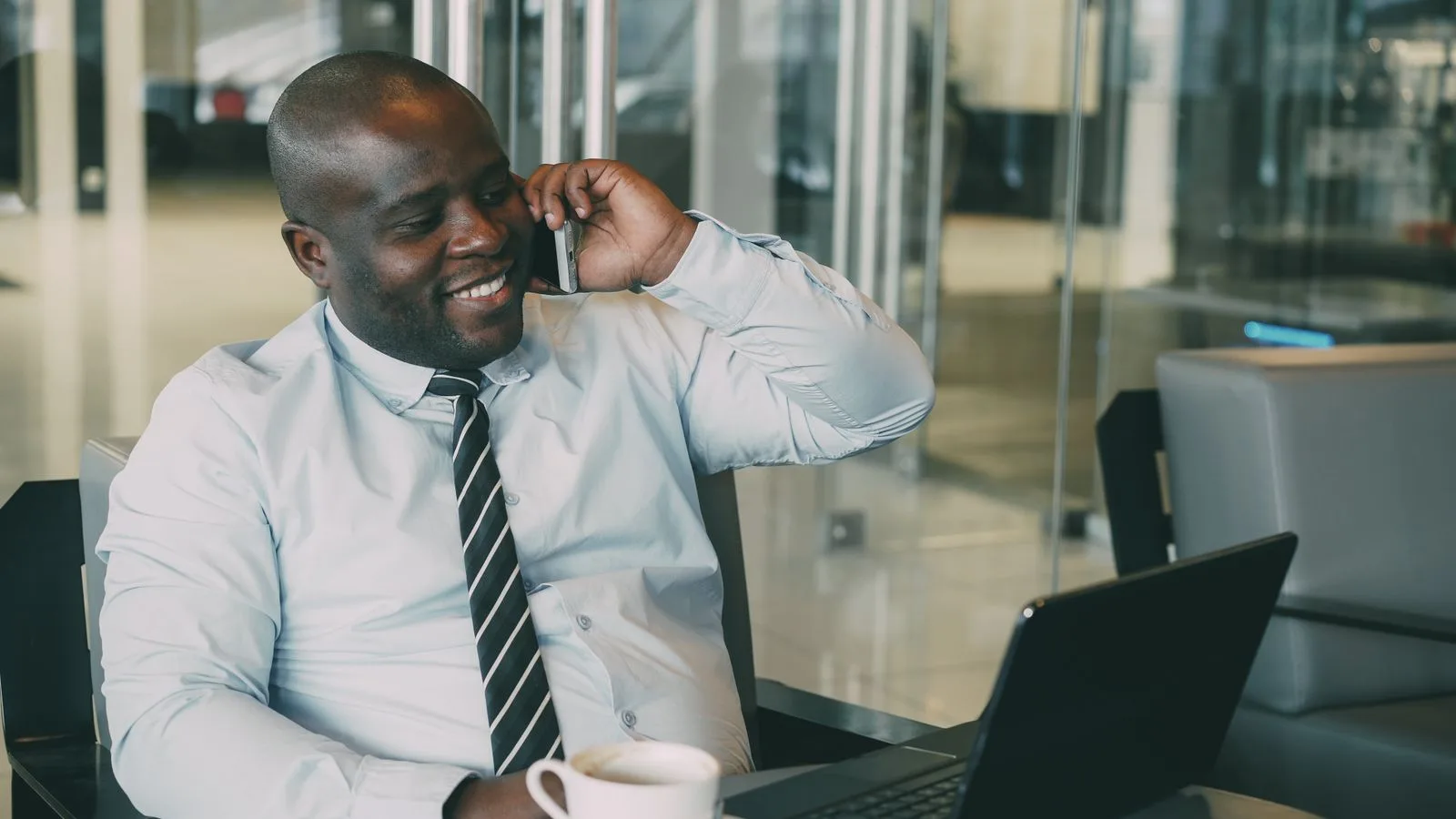 A smiling businessman talking on the phone while working on his laptop, tracking a customer conversation