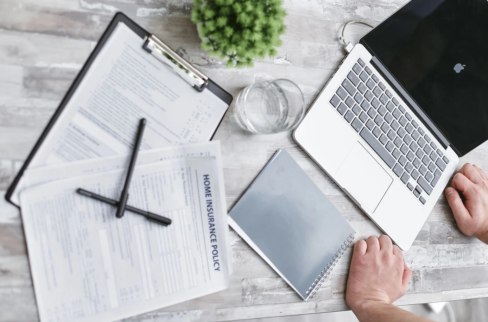 Top view of home insurance policy forms, a laptop, and documents on a desk