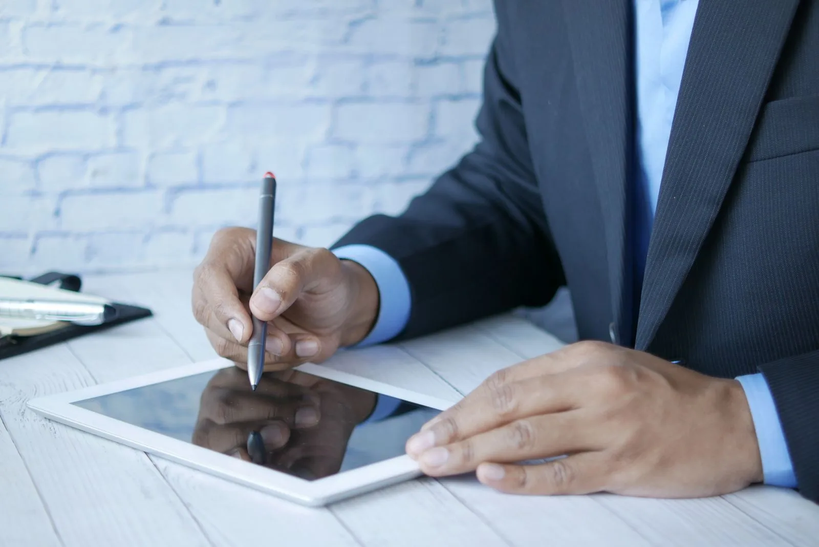 A man in a suit using a stylus to sign on a tablet for business work