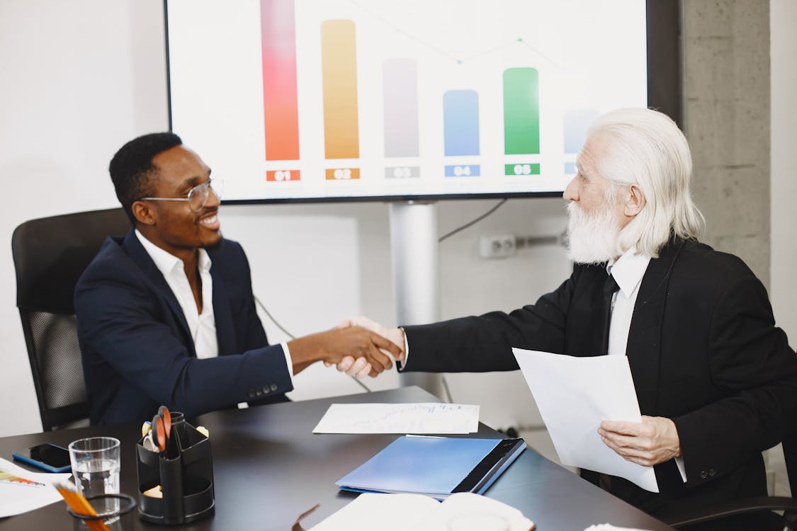 Business leaders shaking hands in an office setting with charts in the background
