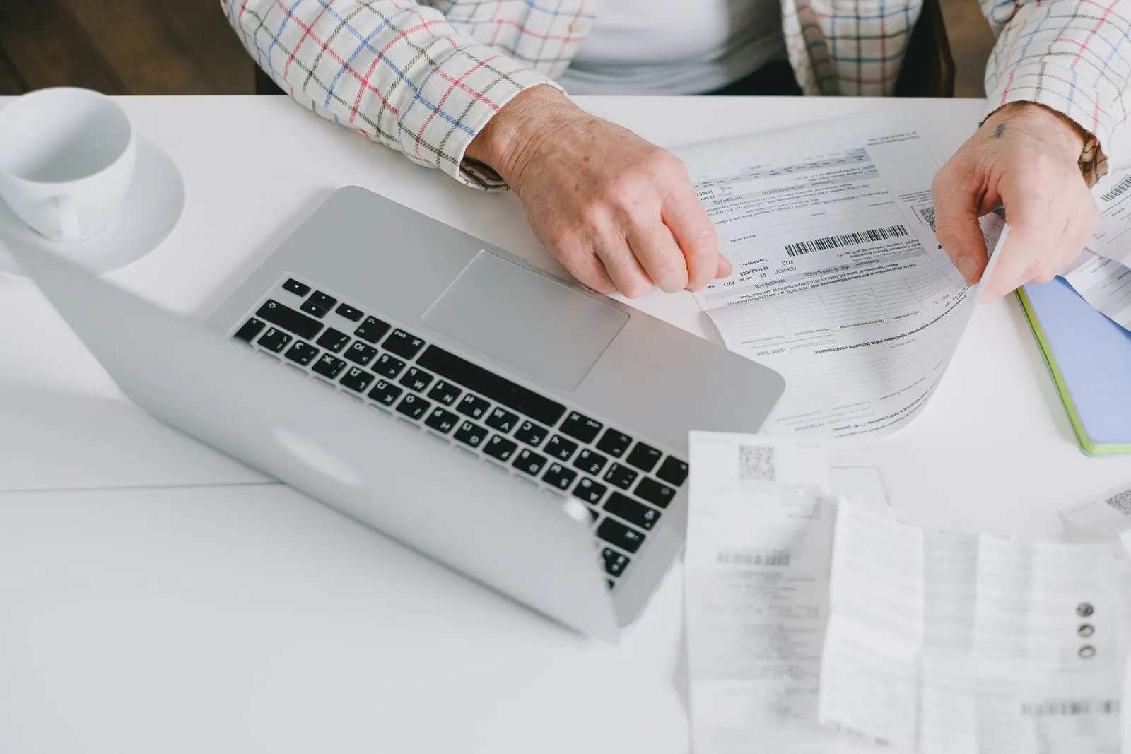 Hands sorting printed claim forms with barcodes next to an open laptop