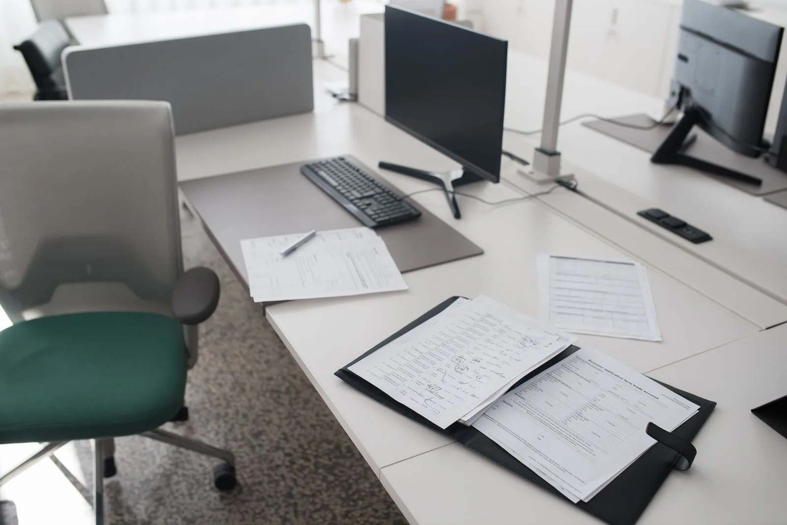 A clean, organized, empty office desk with documents and a computer, chair pushed in