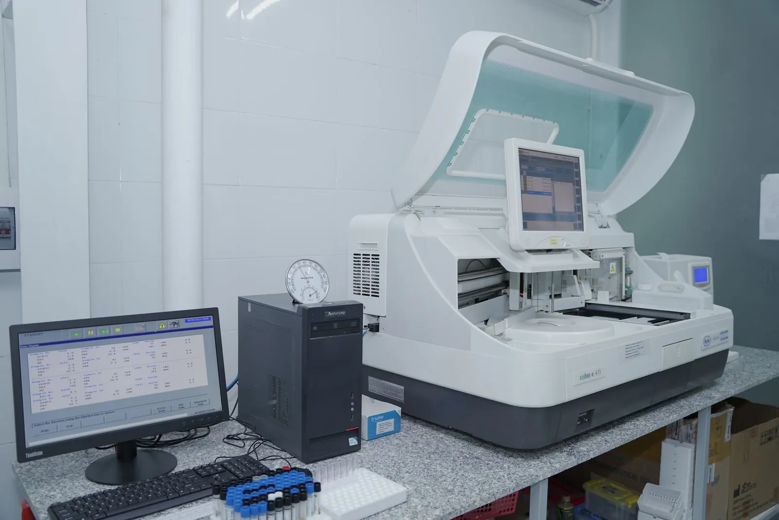 A laboratory analyzer next to a computer showing a results screen