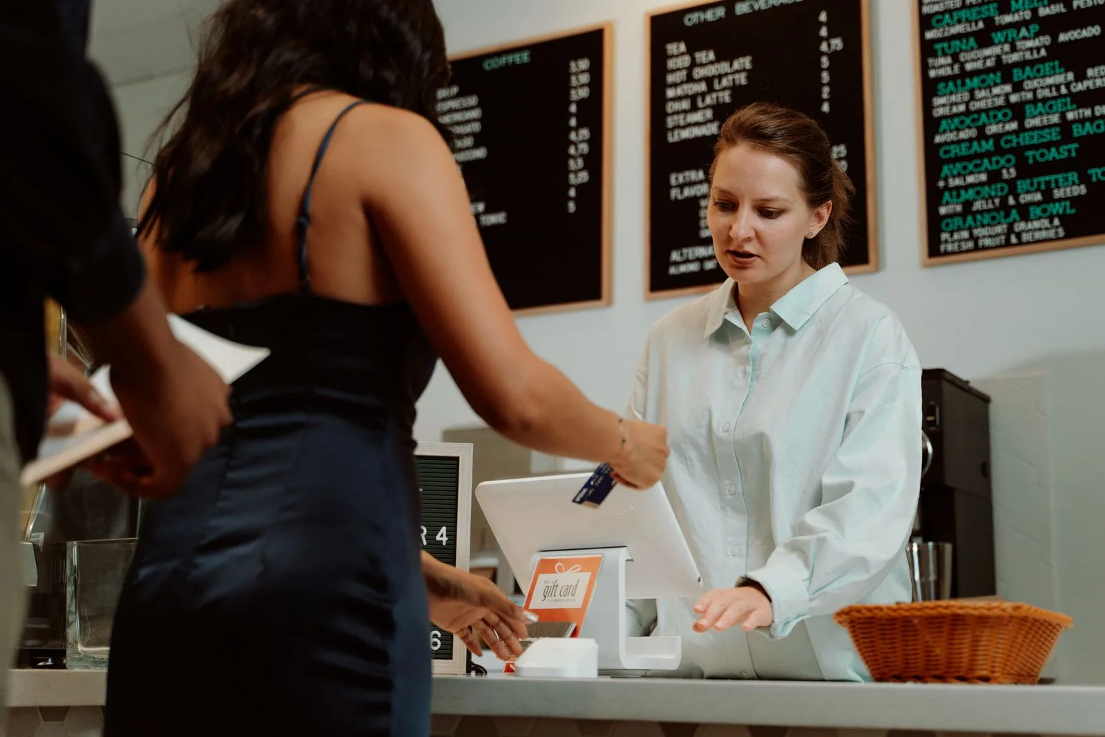 A customer paying with a card at a coffee shop counter while a barista assists