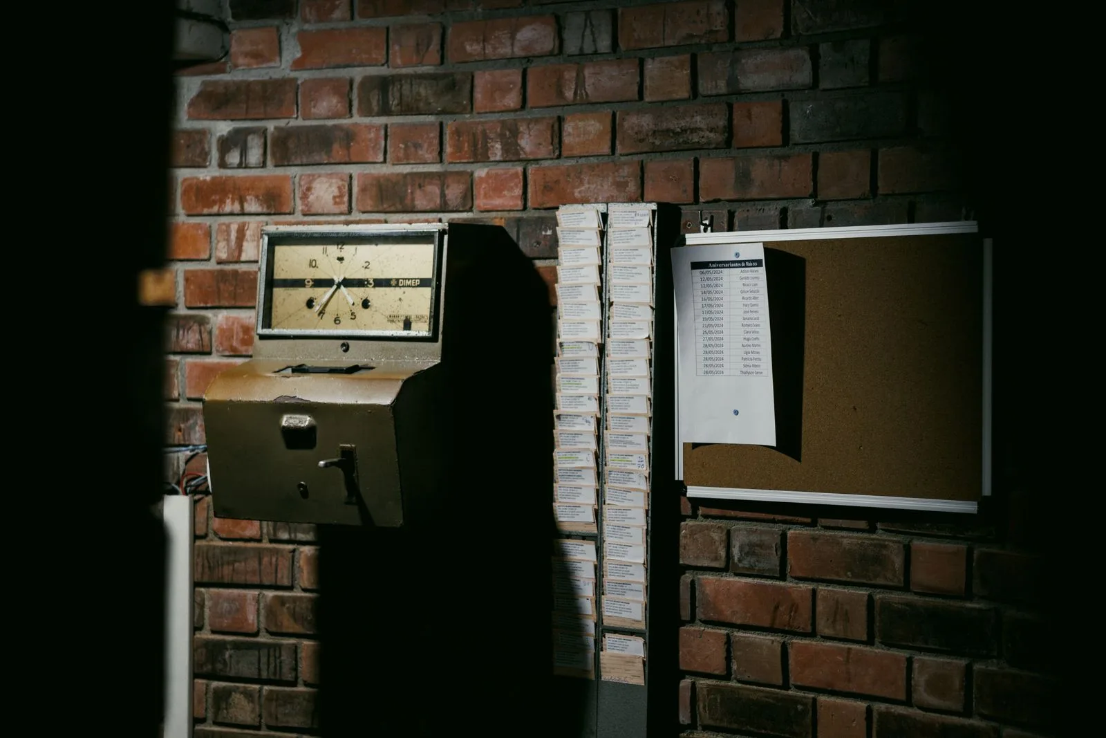 A retro time clock and a stack of punch cards against a brick wall