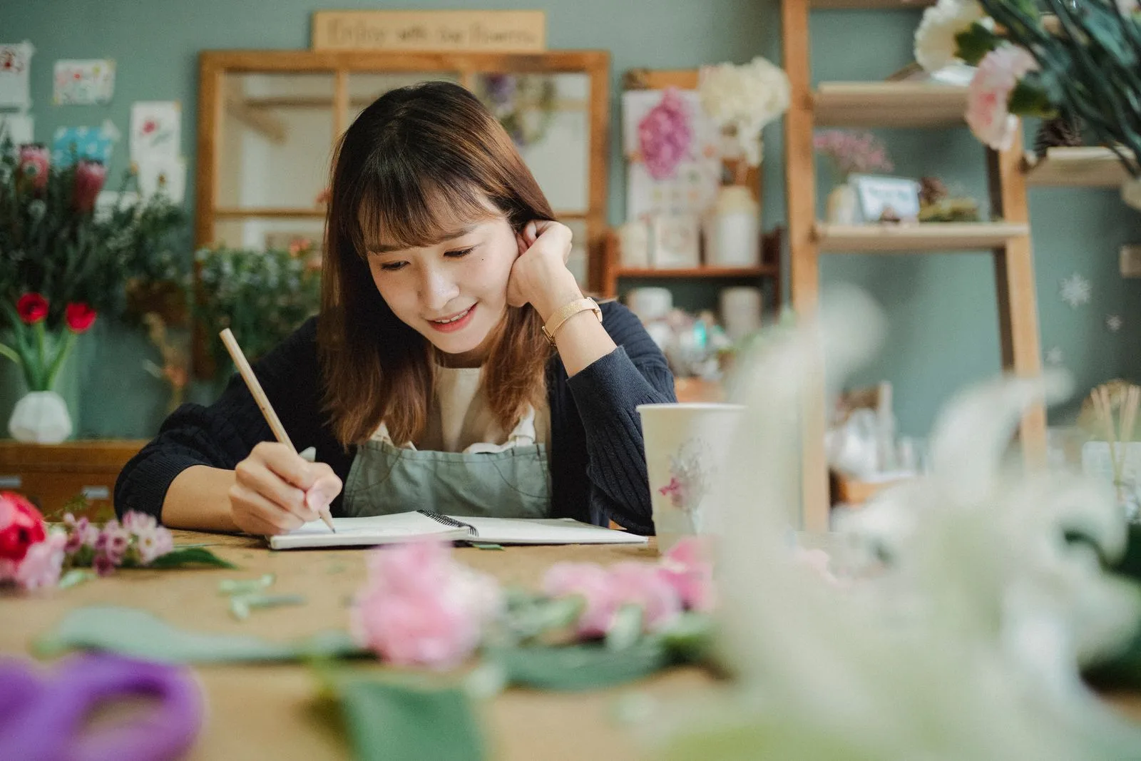 A small business owner in an apron writing notes by hand in her shop