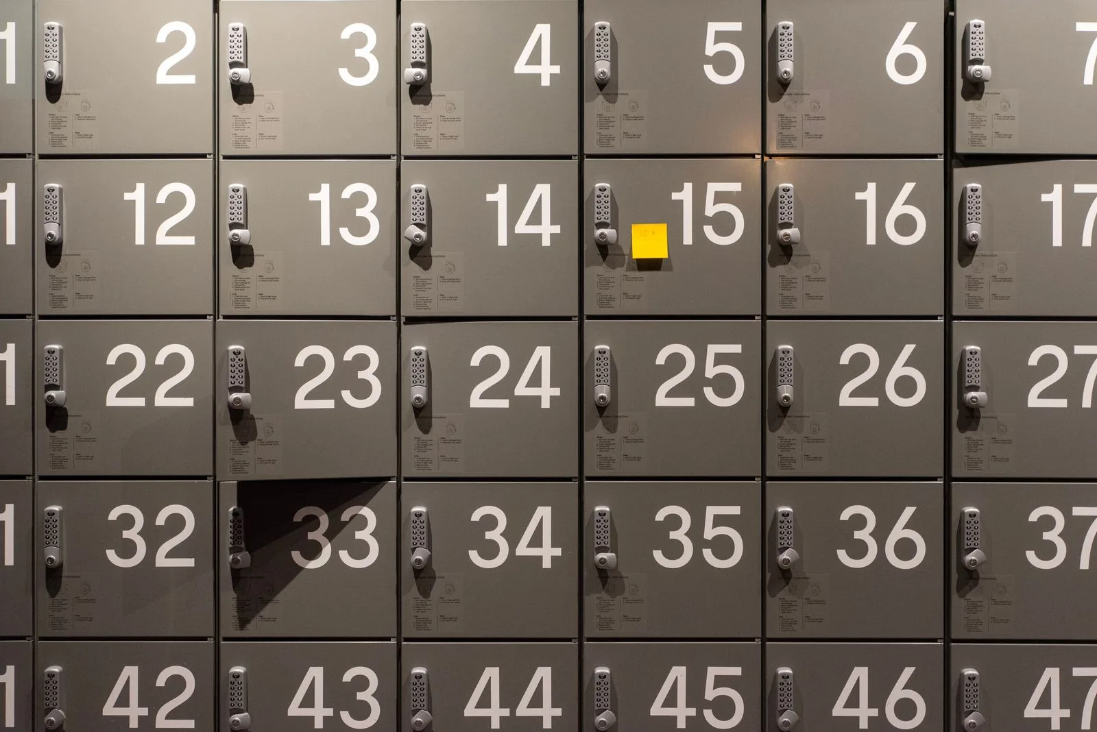 Rows of numbered electronic lockers with a single yellow sticky note attached to one