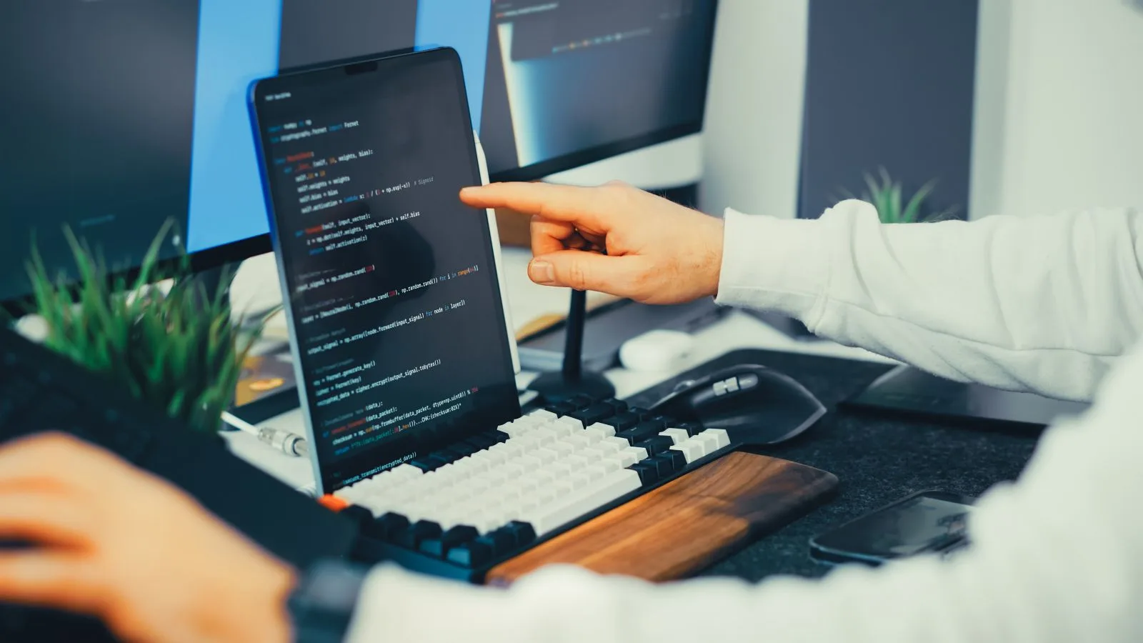 Programmer working on code with a laptop and monitor setup in an office