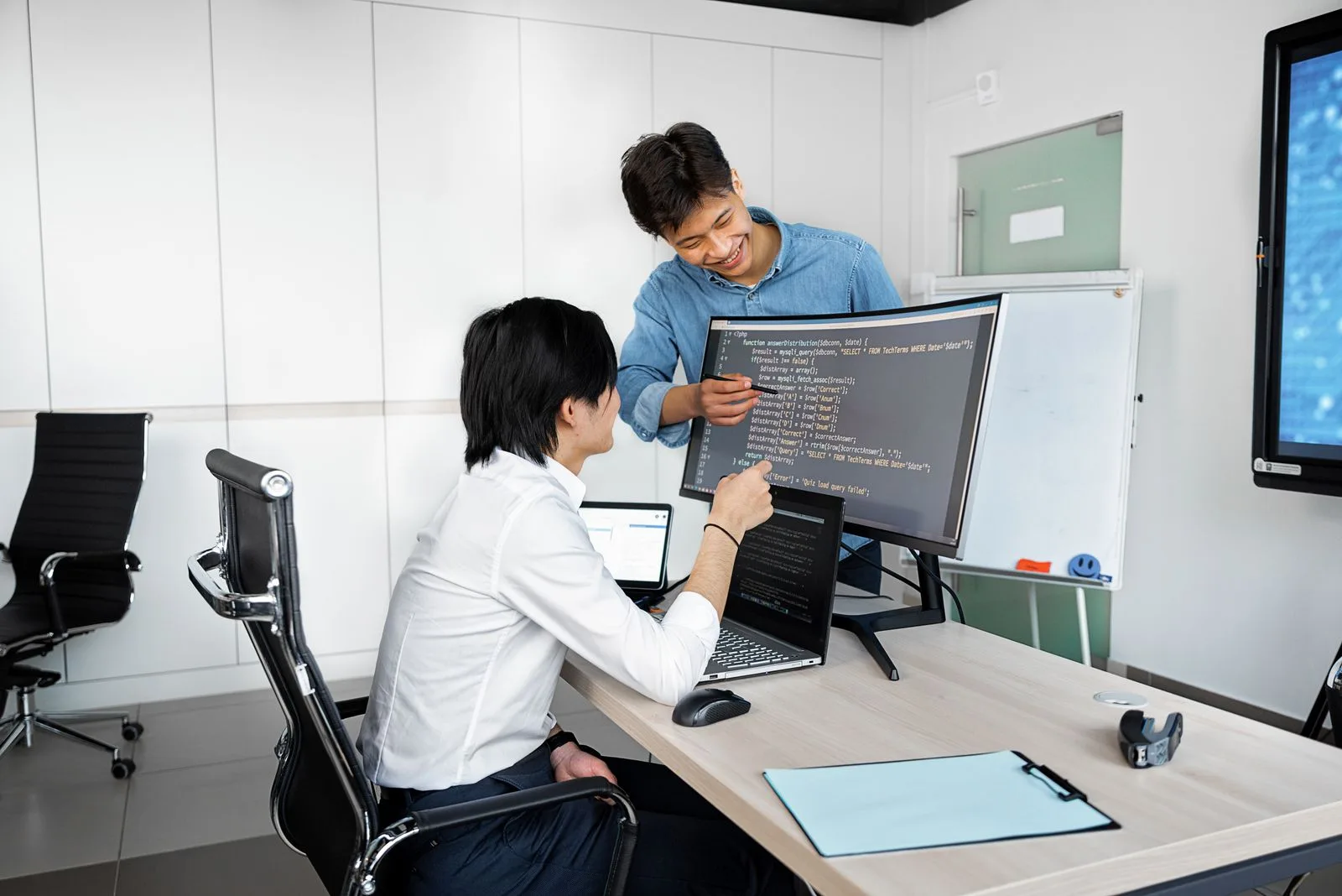 Two professionals collaborating on coding tasks with laptops and monitors
