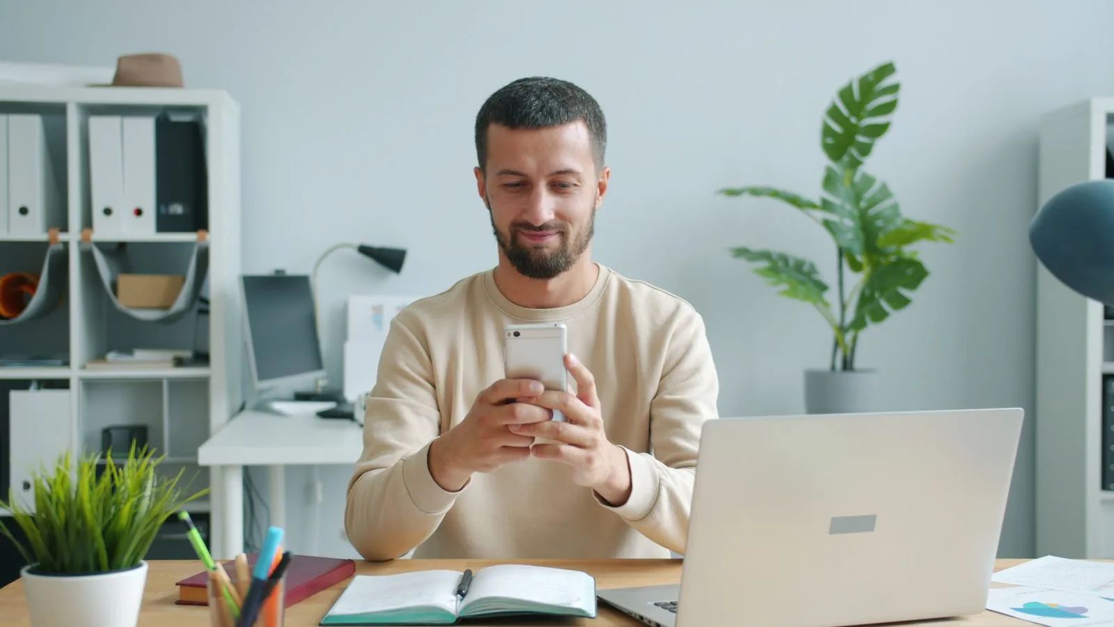 A man at his desk quietly using a smartphone alongside his work laptop