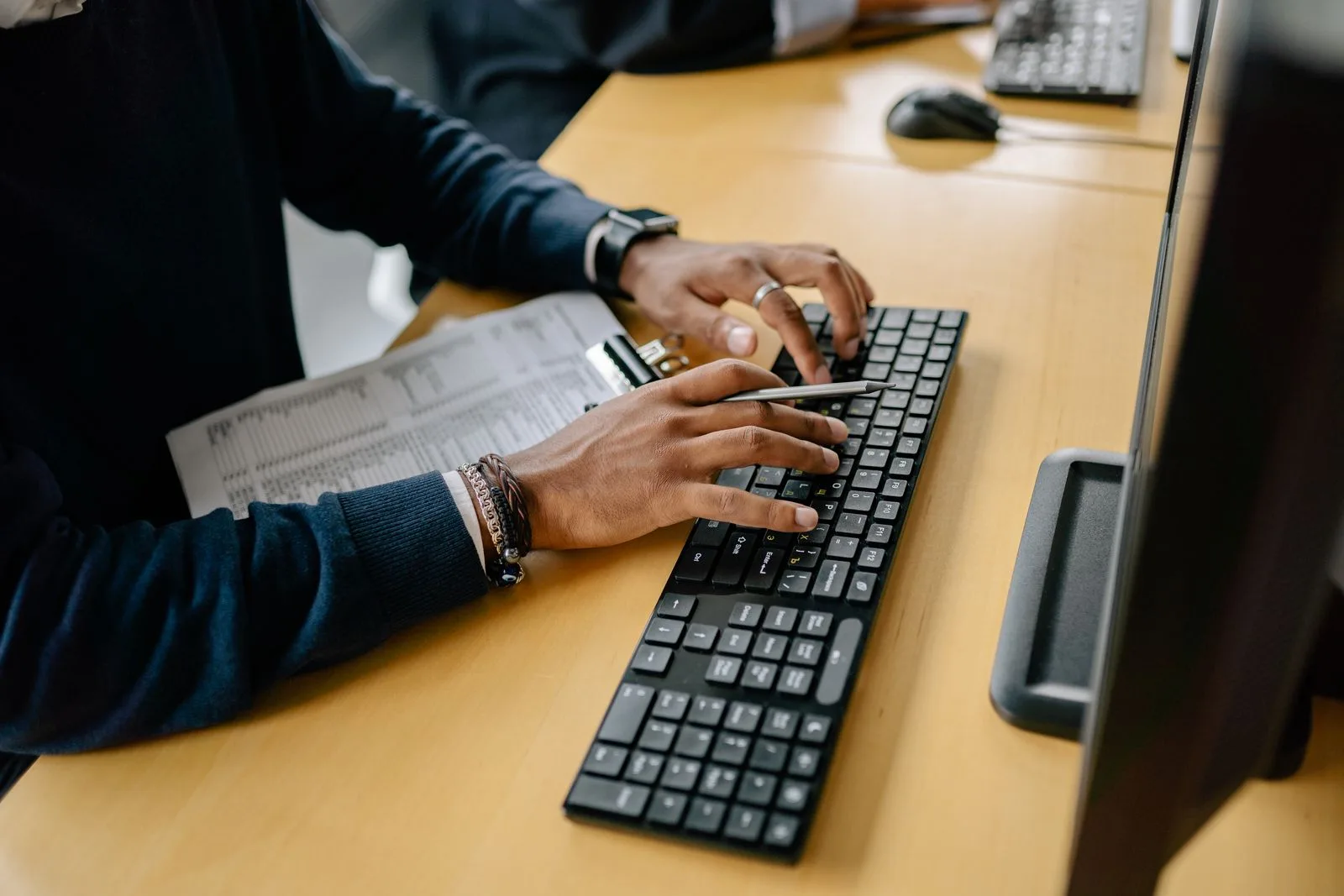 Hands typing on a keyboard with a clipboard nearby, representing repetitive office data entry