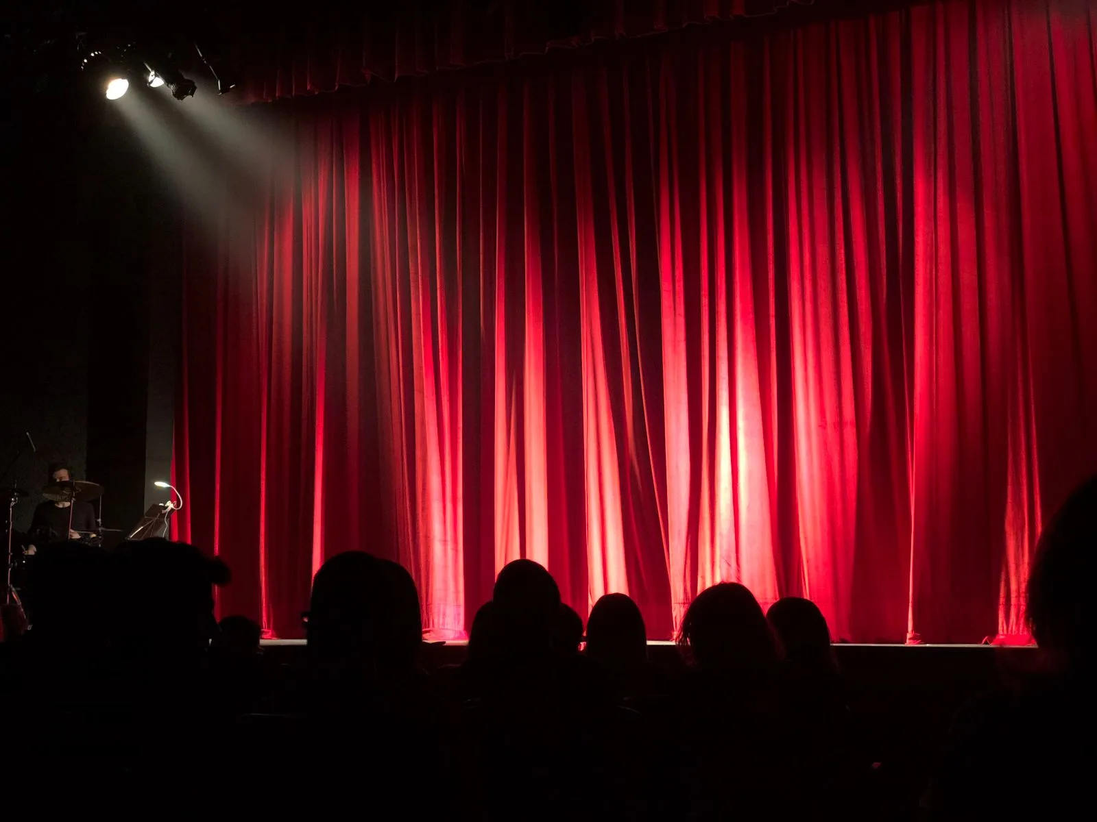 A theater stage with red curtains and audience silhouettes under spotlights