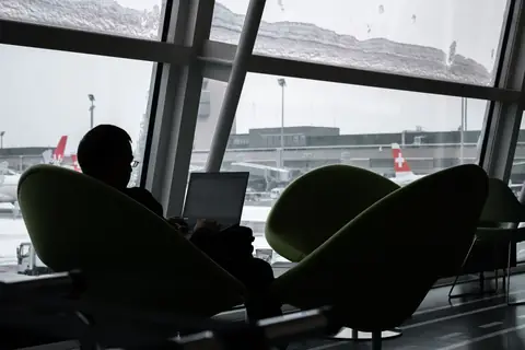 Silhouette of a person working alone on a laptop at an airport lounge