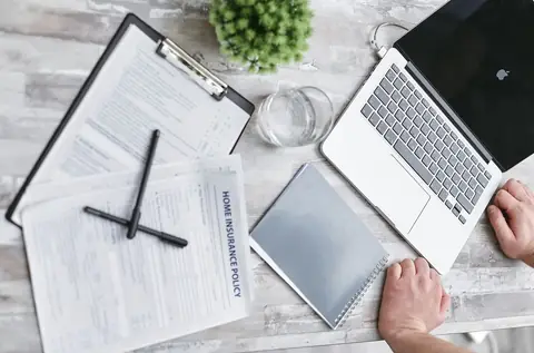 Top view of home insurance policy forms, a laptop, and documents on a desk