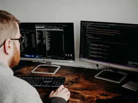 A software developer working on code across dual monitors in an office