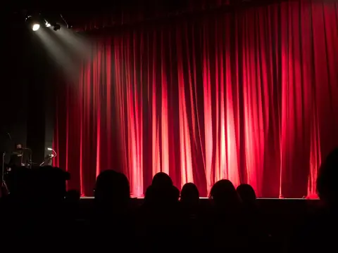 A theater stage with red curtains and audience silhouettes under spotlights