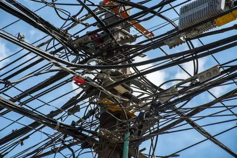 A chaotic tangle of power lines interwoven on a utility pole