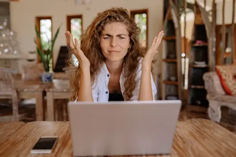 A frustrated woman raising her hands in confusion while looking at her laptop screen