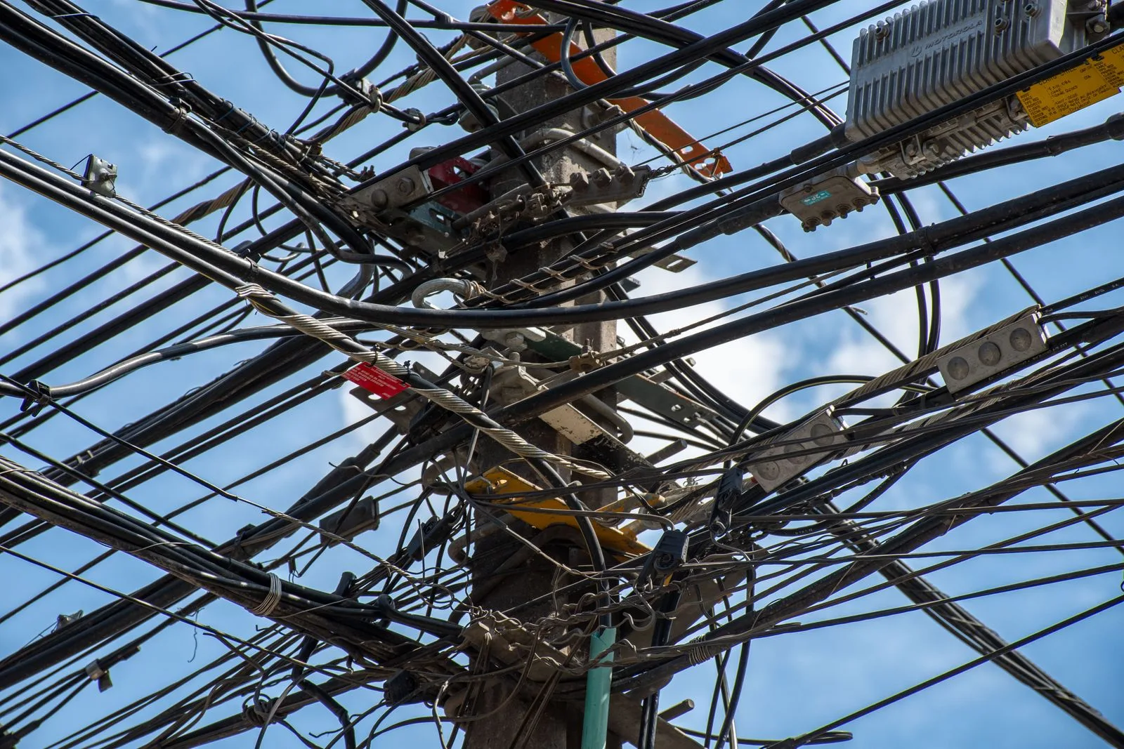 A chaotic tangle of power lines interwoven on a utility pole