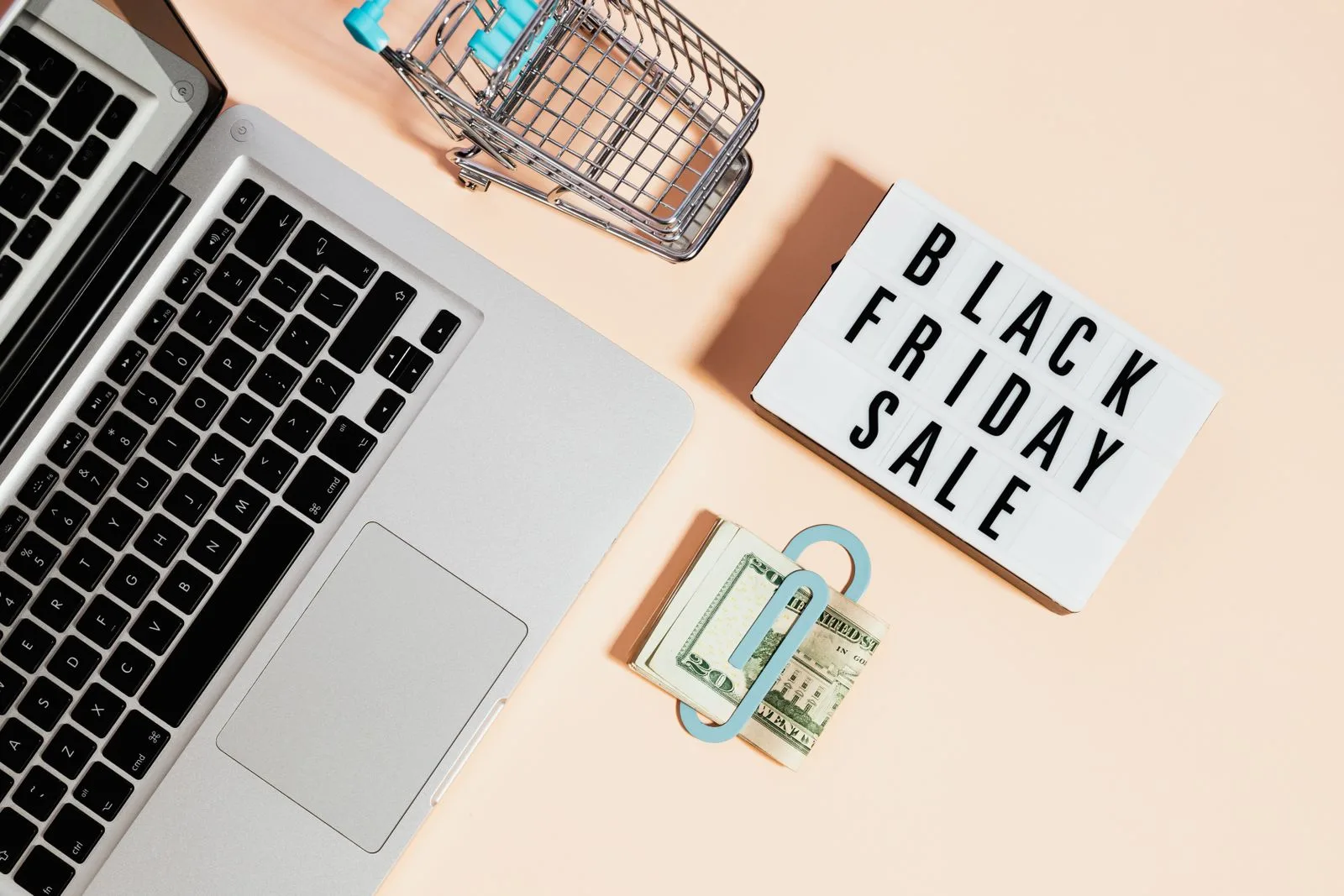 Overhead view of a laptop, shopping cart, and cash surrounded by sale signage