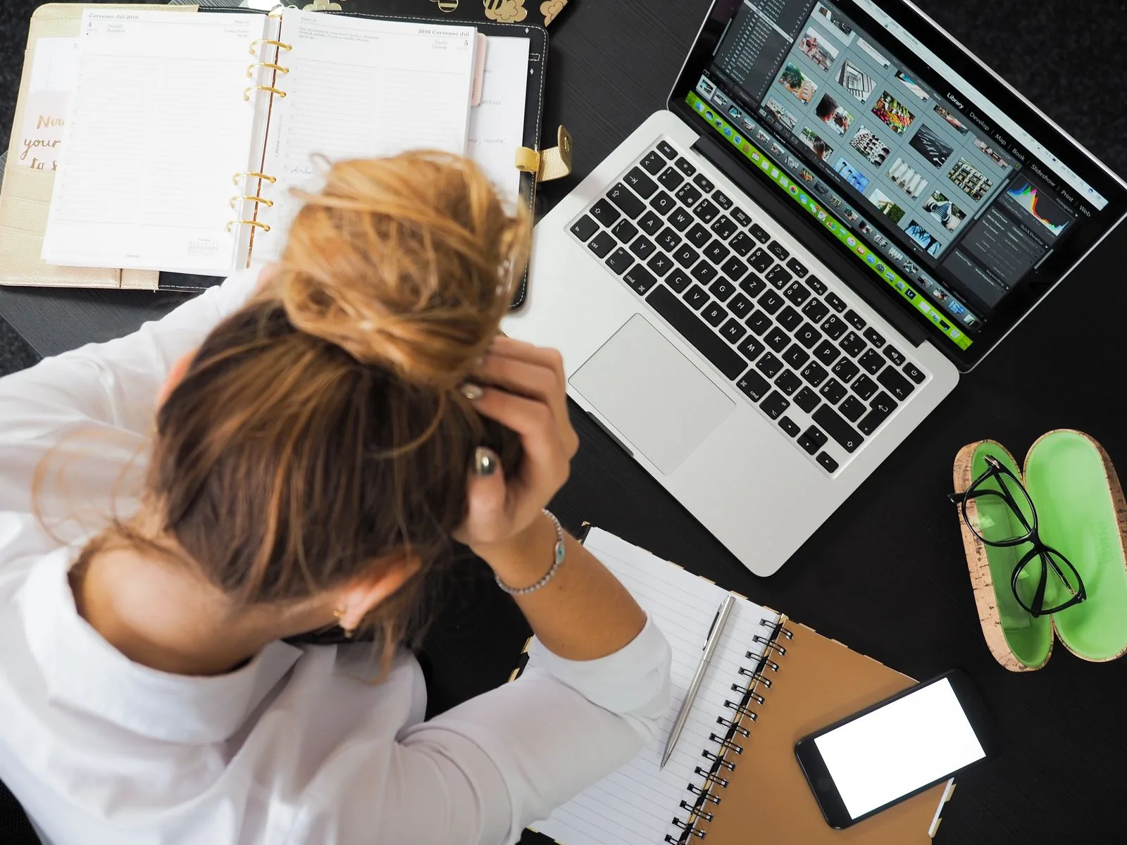 Overhead view of a stressed business owner working at a desk with a laptop, phone, and notebooks