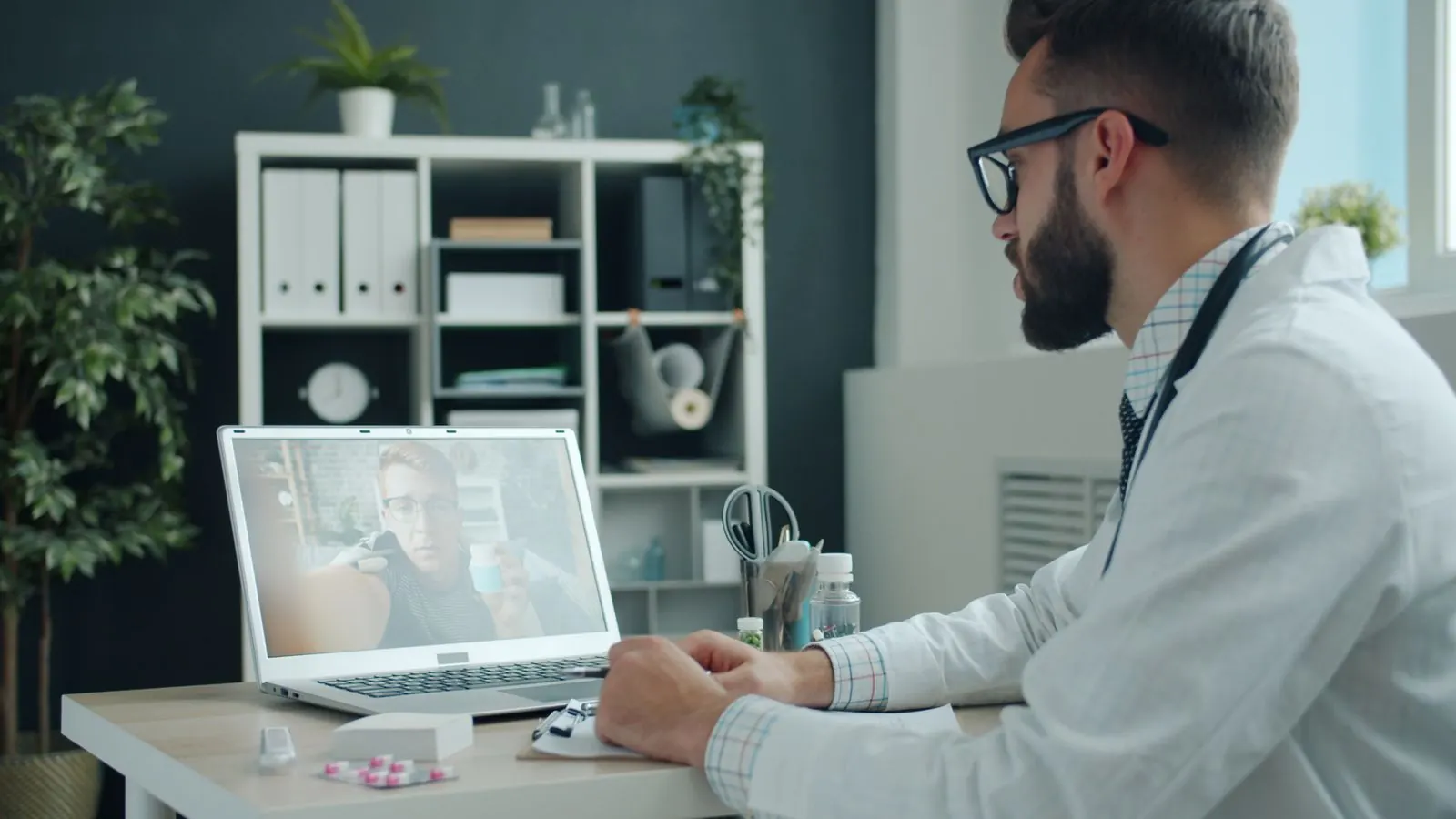 A doctor on a video call with a patient on a laptop in a consulting room
