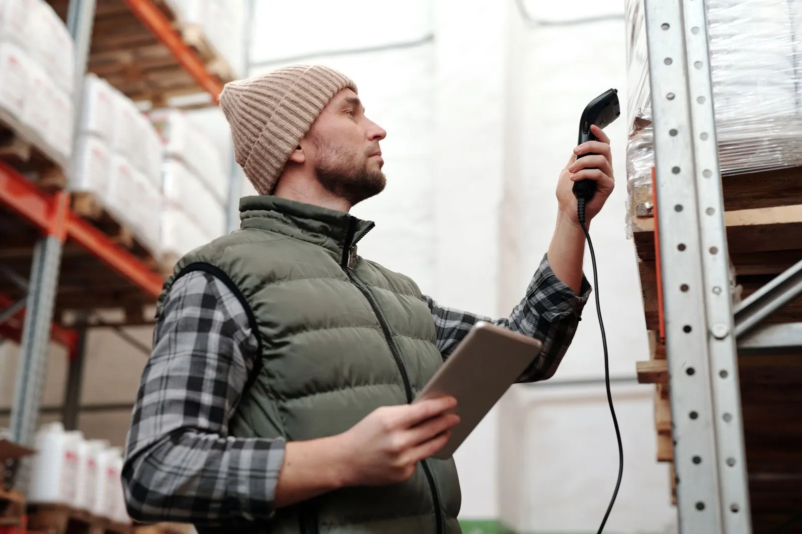 A warehouse worker scanning a shelf with a handheld scanner while holding a tablet